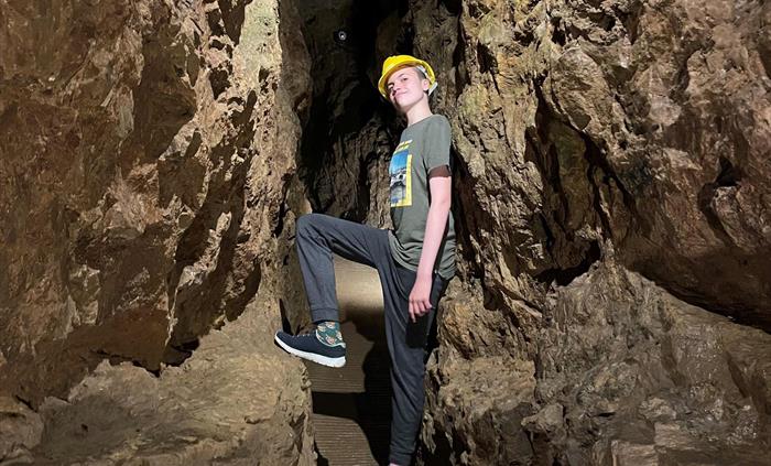A young teen standing in a narrow section of the underground passageway, just a little wider than shoulder width, he is leaning his back against the r